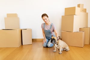 happy-woman-with-dog-and-boxes-moving-to-new-home-PRLJ6R2